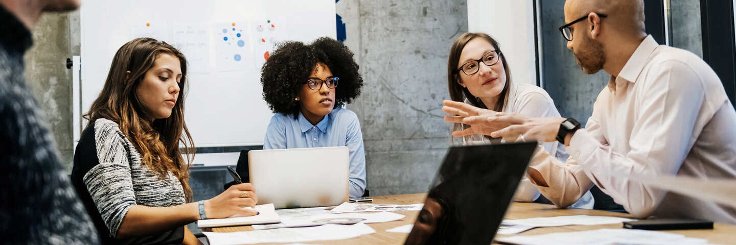 A group of three young women and two men are in a business meeting in a modern day office