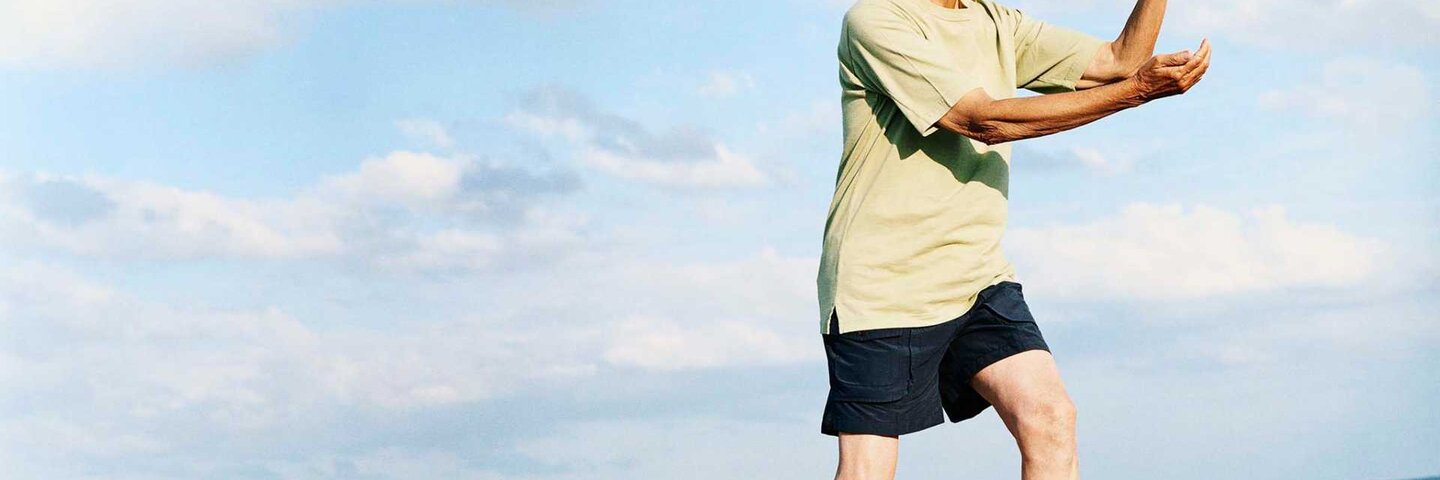 Senior Man Stands on the Beach Doing Tai Chi
