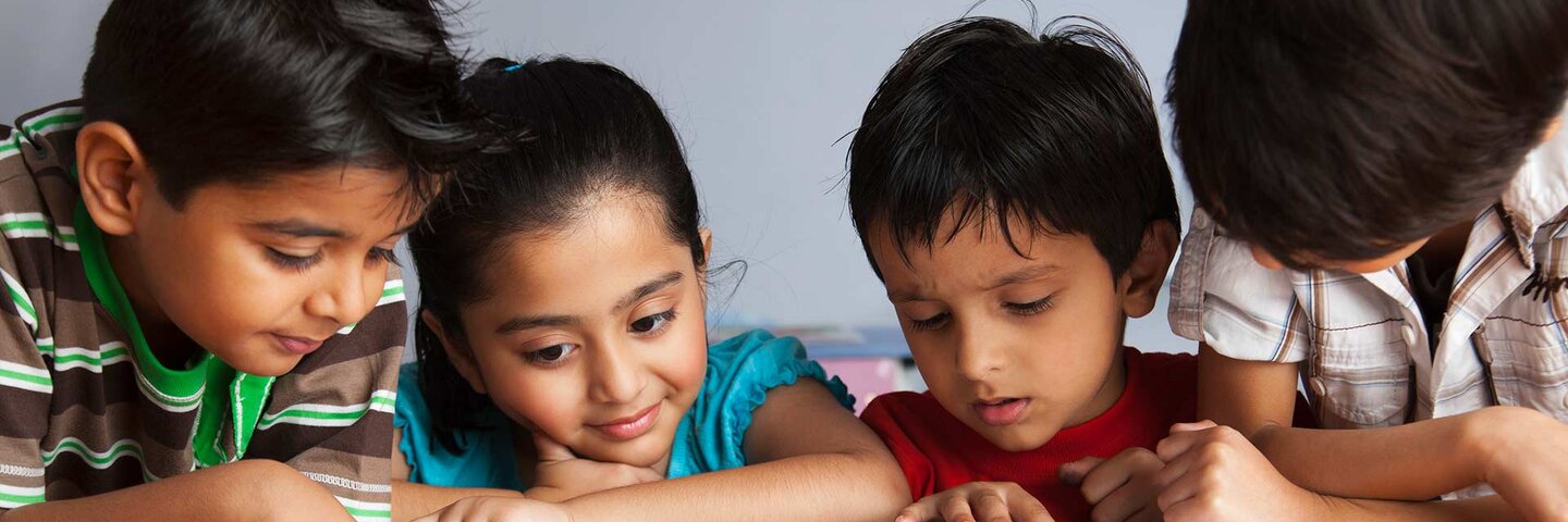 Boys (6-7) and girl (4-5) enjoying reading children's book