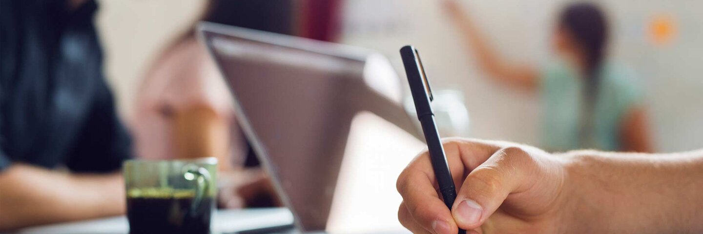Coworkers having meeting at office; close up of hand writing in book
