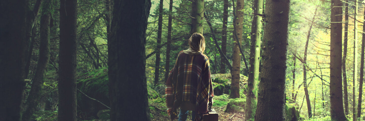 Woman with suitcase walking through the woods