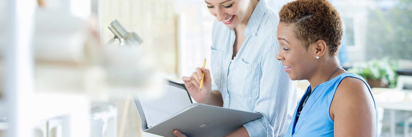 Confident female architects plan a project together. They are looking in a portfolio or calendar as they discuss the details of the project.