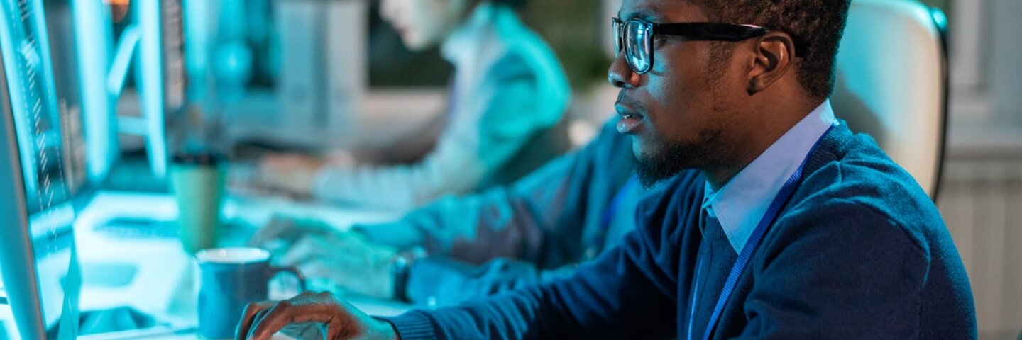 person in front of a computer with another person in the background on a computer